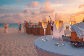 Sunset sunlight closeup glasses of champagne in a restaurant on the coast of a resort in the Maldives. Blurred people having fun at weekend summer night, leisure lifestyle. Outdoors bar beach view