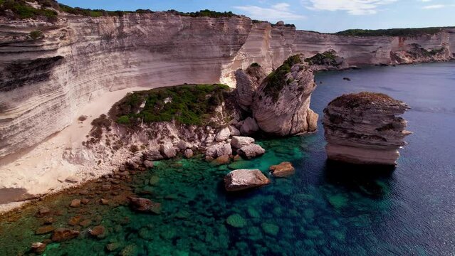 France Corsica Bonifacio aerial drone 4K. Flight over Grain de Sable sea stack rock with motor boats in turquoise water. White limestone cliffs scenery. Luxury Mediterranean travel