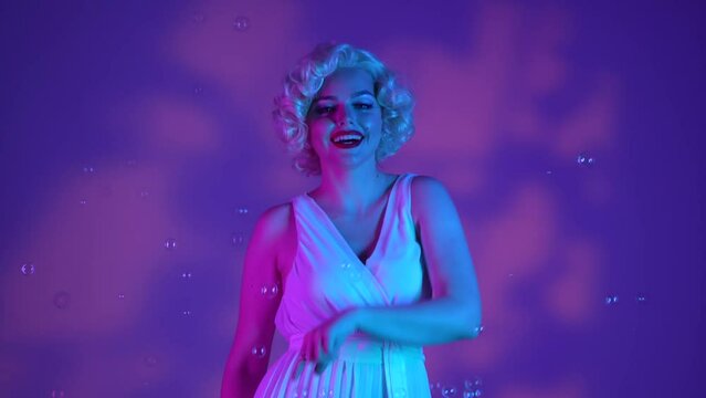 Woman dancing surrounded by soap bubbles, sending air kisses. Woman in the image of on a pink background with highlights, in a studio illuminated with pink and green neon light.