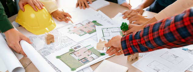 Professional architect cooperate with engineer discussing the use of green design in eco house project on table with blueprint and architectural equipment scatter around. Closeup. Delineation.