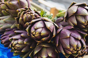 Close up of organic fresh violet artichokes in a box at outdoor farmers market. Cynara cardunculus var. Scolymus. Vegan food and healthy nutrition concept. Artichoke for sale in the street of Italy.