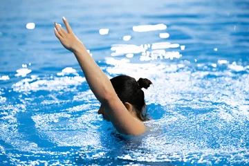 Tuinposter a synchronized swimming sportswoman practice new moves in the water of swimming pool alone © Mihail