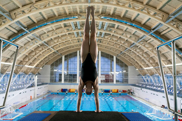 a girl stands on her hands on the edge of a springboard, preparing to jump into the water
