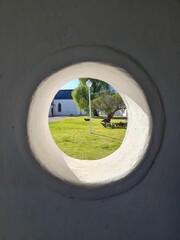 a circular hole in a wall with the view of a church through