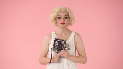 Portrait of woman with retro video camera in hands close up. Woman looking like in studio on pink background.