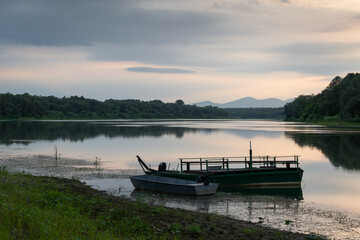 Fototapeta na wymiar Landscape with moored boats in river against mountain silhouette in distance and cloudy sky