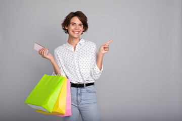 Beautiful woman with shopping bags and smart phone is pointing away. Black Friday, consumer, buyer,...