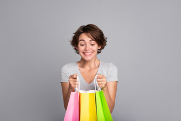 Beautiful excited woman with short hair in t-shirt looking inside colorful shopping bags. Shopping, black Friday, consumer, buyer, sale, store, payment, online buying, discount, purchase, mall