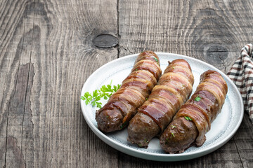 Appetizing sausages wrapped in bacon and grilled on white plate on wooden table