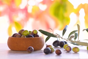 
Olives on wooden table in the garden, olive oil in glass jug and autumn leaves background