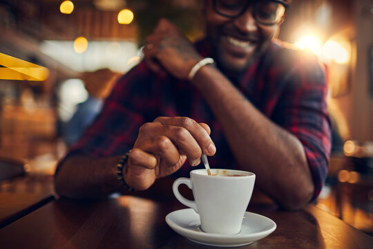 Young man holding spoon in mug at cafe