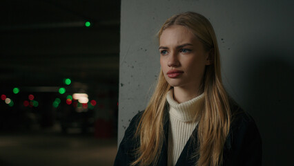 Portrait serious Caucasian 30s woman businesswoman driver car owner posing on darkness background female entrepreneur lady looking front at camera standing in underground car parking alone lonely girl