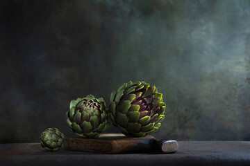 Artichokes on a wooden board. Dark background. Space for copying.