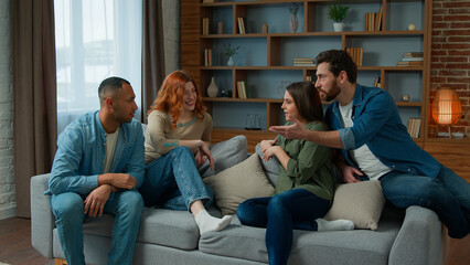 Ethnic friends sit on couch in living room diverse colleagues teammates women girls and men guys smiling talk discuss share plans friendly discussion dialogue laugh friendship weekend meeting at home