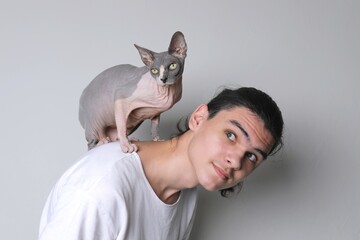 Teenager and cat. Hairless cat sits on the back of teenage boy with long hair