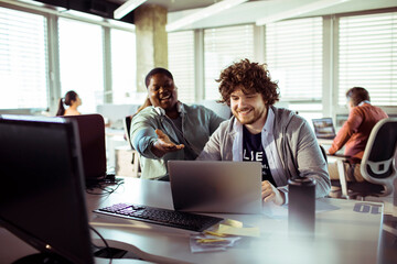 Two young office workers looking at laptop working on project together