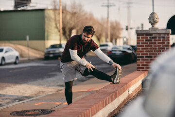 Young man stretching foot before jogging in sports clothes and headphones