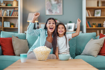 Happy young mom and her daughter watching football game on television - obrazy, fototapety, plakaty