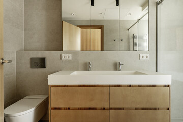 Front image of a beautiful modern bathroom with gray stone-like tiles, built-in mirror on the wall,...
