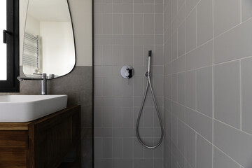 Small modern bathroom with gray stone effect tiles, mirror on the wall, white porcelain sink...