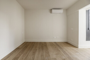 Empty room with plain off-white painted walls, wooden floors and an air conditioner on one wall