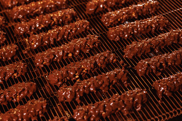 Sweets waffles with nuts and chocolate on conveyor line for bake production. Process cocoa glazing....