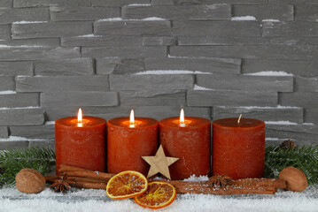 Dritter Advent: Drei brennende Kerze mit Zimtsangen und Orangenscheiben vor einer Mauer mit Platz...