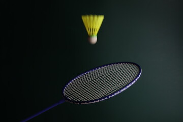 Playing badminton with a racket and shuttlecock in a dark green background. Yellow Shuttlecock in movement.