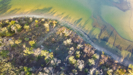 Curved shoreline and remote waterfront primitive camping sites with tents at Isle du Bois Ray Roberts Lake State Park lush green tree forest near Denton, Texas, US aerial view