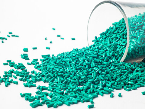 Turquoise masterbatch granules of cold cut type, placed in a glass cup on a white background, this material is used as a colorant for products in the plastics industry