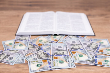 An open book of the Bible on the table. Dollar banknotes. Choice: Wealth or God. It is difficult...