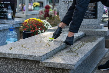 Preparing a grave for All Saints' Day celebrated on November 1st, a woman cleans and washes a marble tomb using a special cleaning solution, brush, cloth, and water. The tomb is clean. - obrazy, fototapety, plakaty