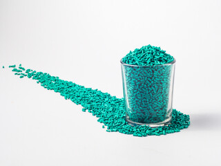 Turquoise masterbatch granules of cold cut type, placed in a glass cup on a white background, this...