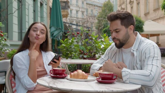European young couple in city cafe woman smiling laughter emotional texting smartphone ignore man fixed gaze distant frustrated relationship problem indifference outdoors breakfast internet addiction