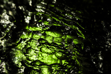 Tektite glass green texture. Moldavite gemstone close up. Rough surface.
