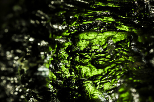 Tektite glass green texture. Moldavite gemstone close up. Rough surface.