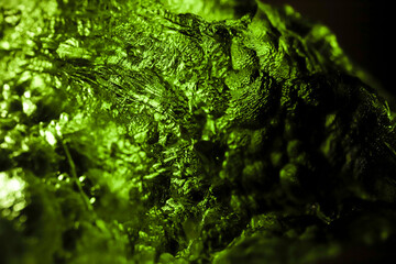 Tektite glass green texture. Moldavite gemstone close up. Rough surface.