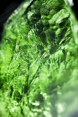 Tektite glass green texture. Moldavite gemstone close up. Lens flare. Light beam. Rough surface.