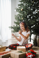 Girl listening music with earphones while unpacking gifts. Celebrating Christmas at home.