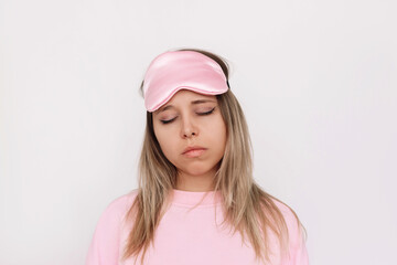Young sleepy blonde woman in a pink pajamas and sleep mask on her forehead with her eyes closed isolated on a white background. Insomnia, sweet dreams. Falling asleep in the day