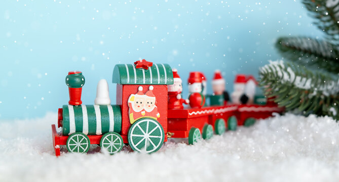 A red and green train stands on the snow on a blue snowy background. Christmas and New Year celebration concept, background