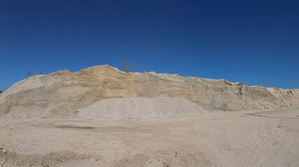 Fototapeta na wymiar piles of white stone and sand at a mining site, on a sunny day, against a blue sky, limestone quarry with hills of extracted rock, industrial lime mining outdoors
