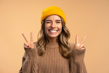 Cute smiling beautiful woman winking wearing stylish yellow hat showing victory sign isolated on...