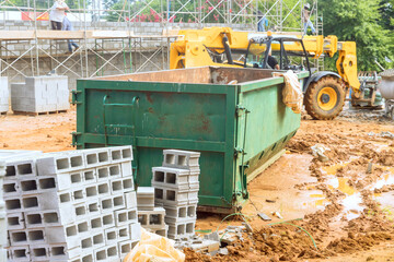 An empty dumpster for construction waste debris near construction site is loaded up with debris