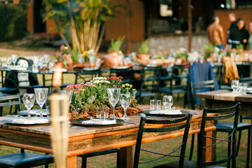 Outdoor dining setup for a sophisticated event featuring crystal glassware, polished plates, and a rustic wooden centerpiece surrounded by fresh potted herbs
