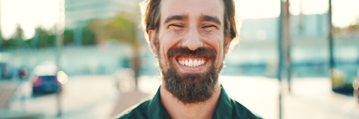 Closeup portrait of smiling man with a beard on an urban city background. Frontal close-up of happy...