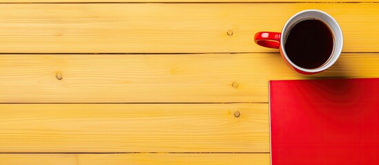A wooden surface showcases a vivid yellow cup along with playful toys and a vibrant red notebook accompanied by a crisp white sheet of paper and a trusty pen - Powered by Adobe