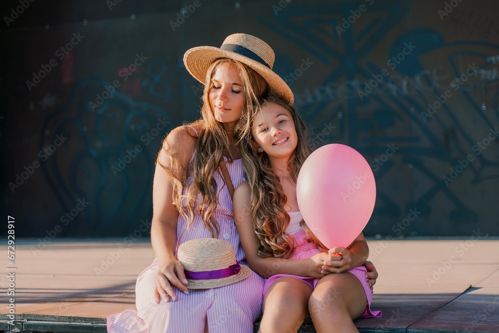 Wall mural Portrait of mother and daughter in pink dresses with flowing long hair against the black backdrop. The woman hugs and presses the girl to her.