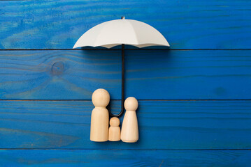 Umbrella and wooden family figures on wooden background, top view. Insurance coverage concept.