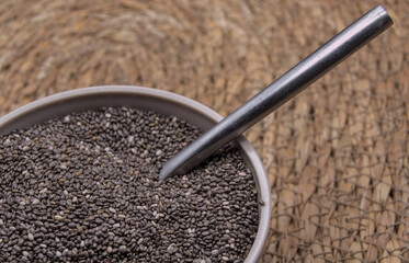 Chia seeds in a light brown bowl, metal spoon on a natural fiber blanket.
